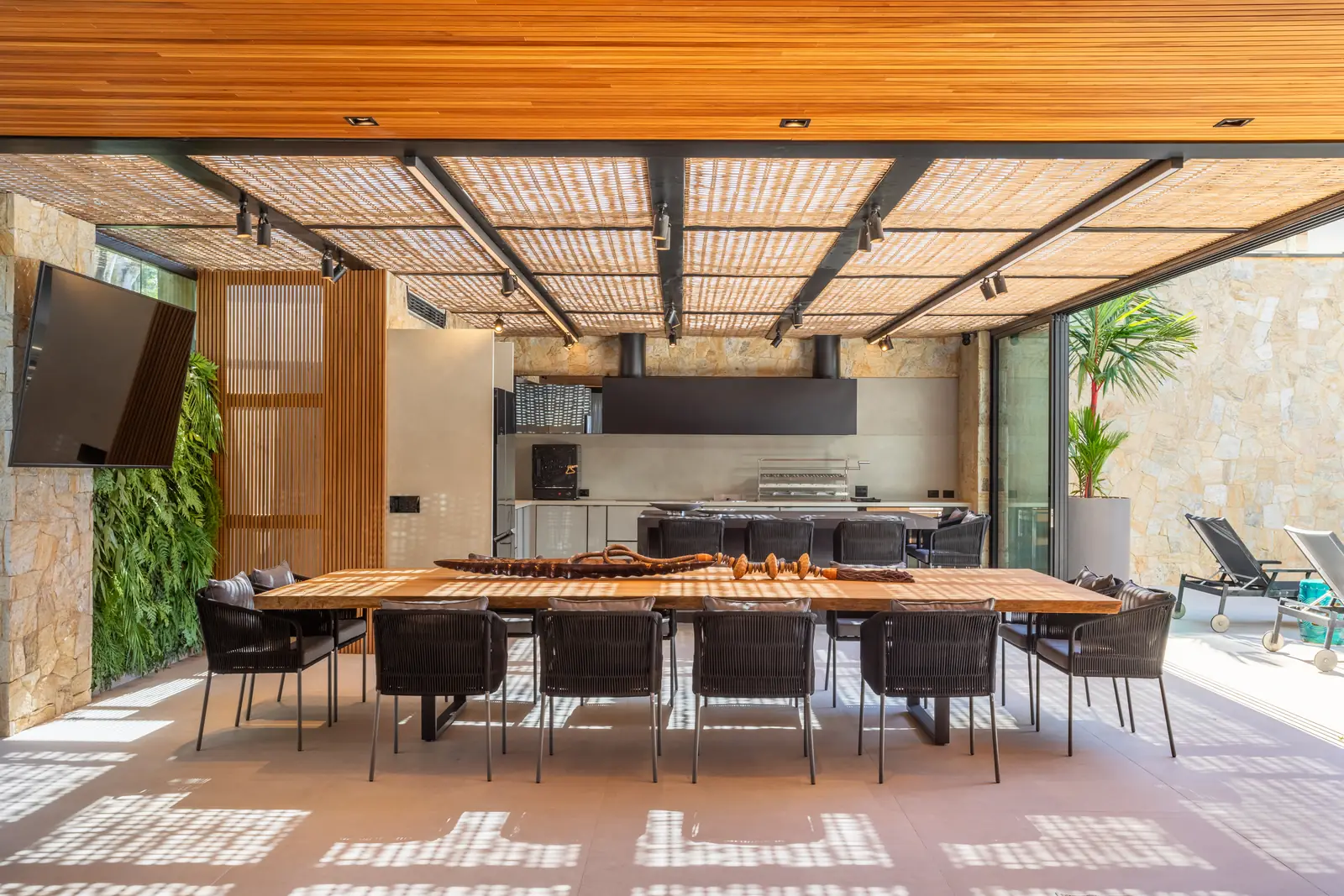 Área gourmet com mesa de madeira maciça, pergolado e jardim vertical