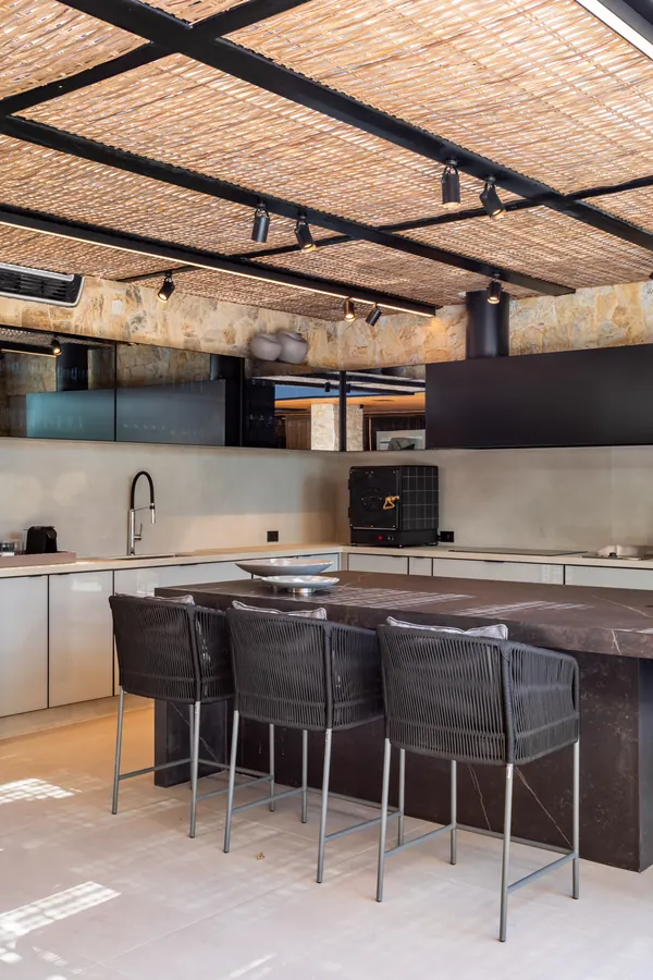 Cozinha da área gourmet com ilha em pedra escura e banquetas