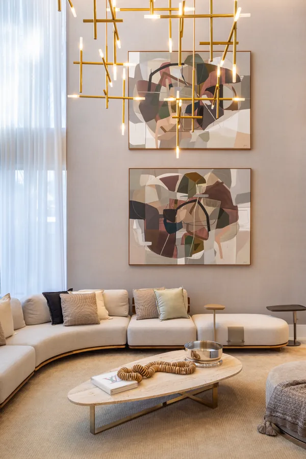 Sala com pé-direito duplo, sofá curvo e quadros abstratos