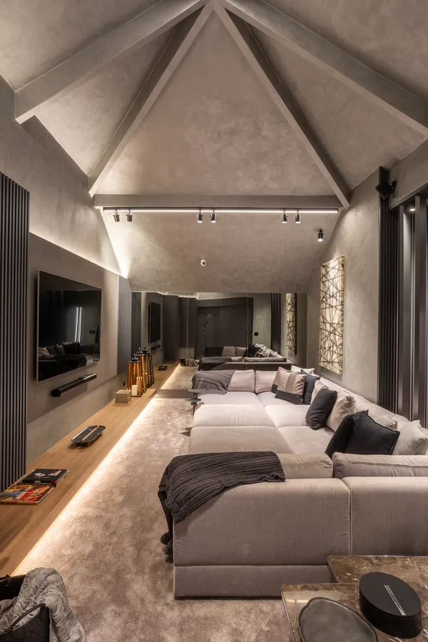 Sala de cinema com teto inclinado, sofá modular e rack em madeira iluminado