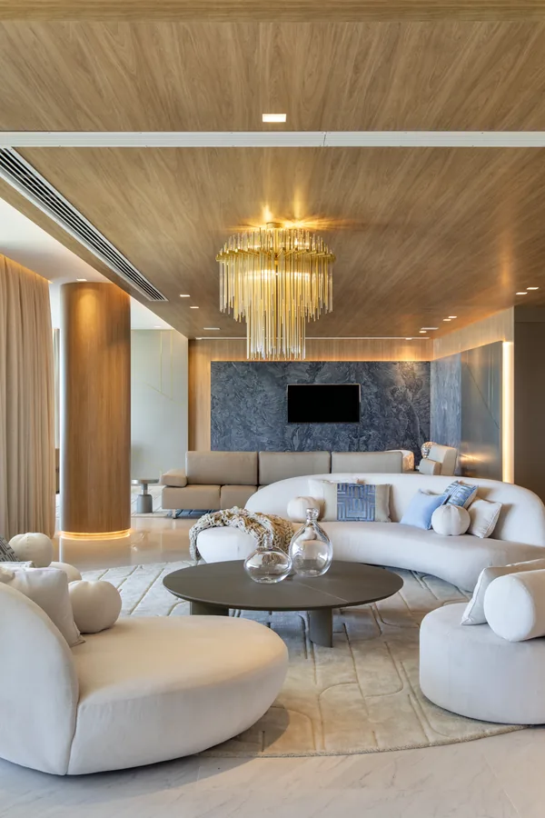 Living com forro em madeira, lustre de cristal, painel em pedra e sofá curvo