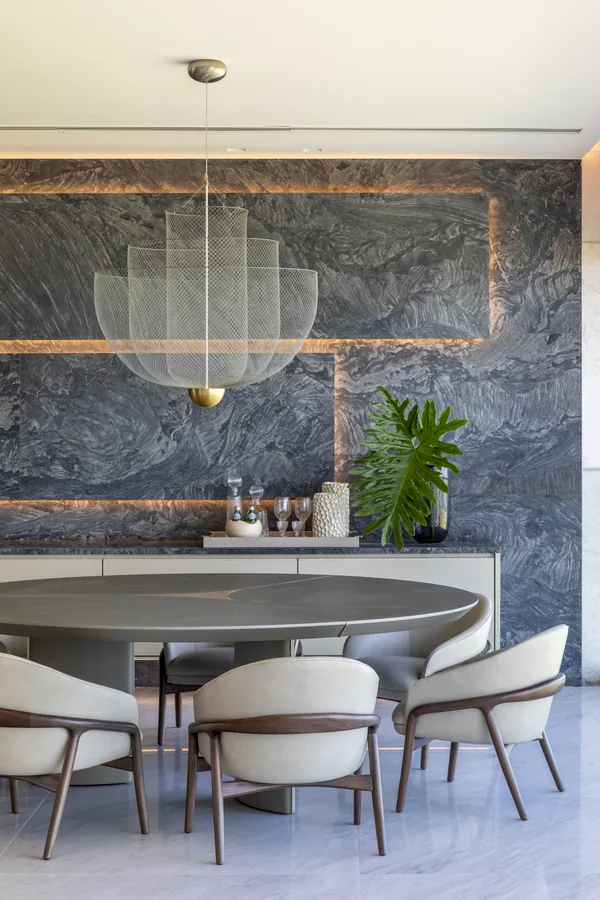 Sala de jantar com painel em pedra azulada, frisos iluminados e mesa redonda