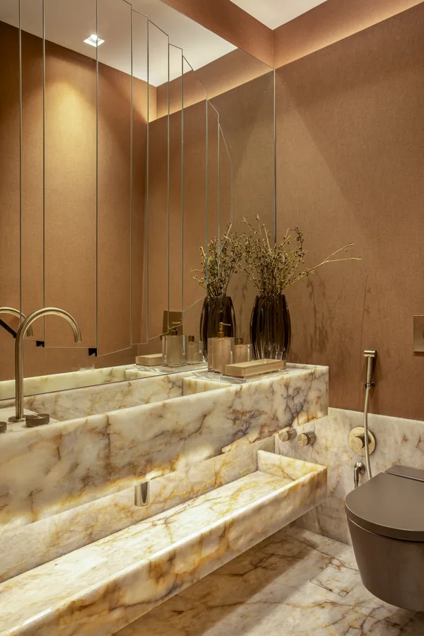 Lavabo com bancada em ônix retroiluminada e paredes em tom terracota