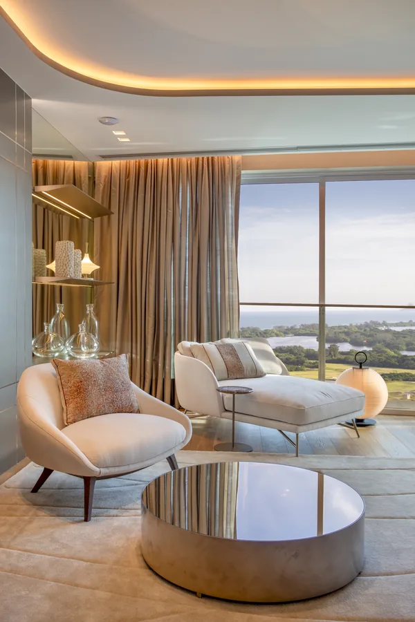 Suíte com estar junto à janela, cortinas e mesa de centro espelhada