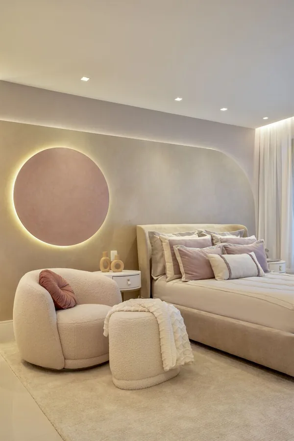 Quarto com painel curvo retroiluminado, nicho circular rosado e poltrona em bouclé