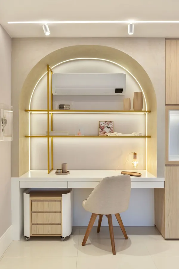 Home office em nicho de arco com prateleiras douradas iluminadas e bancada branca