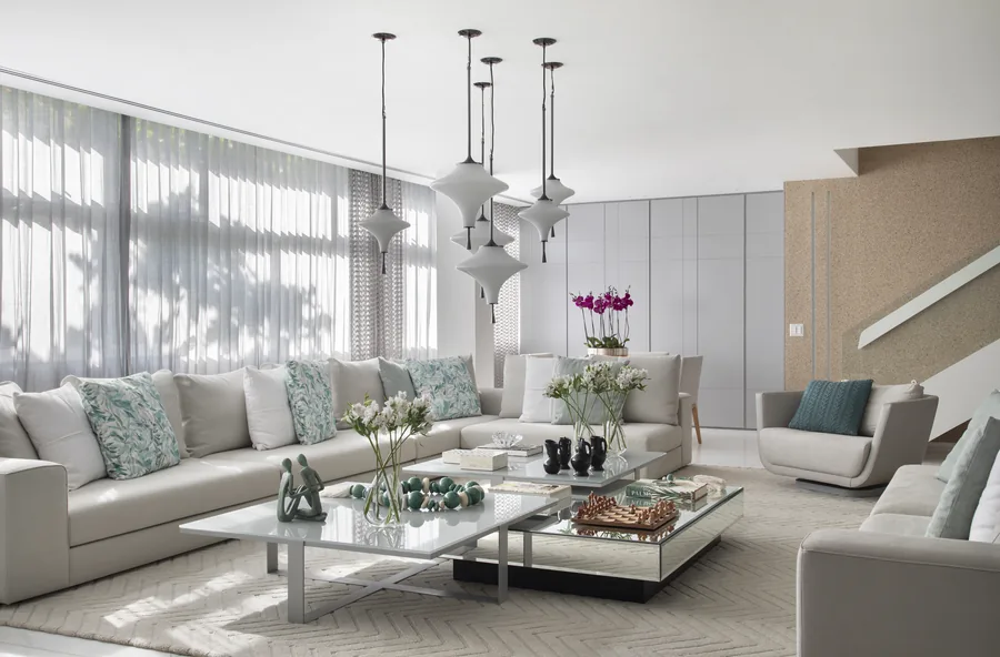 Living amplo com sofás claros, pendentes de vidro e cortinas