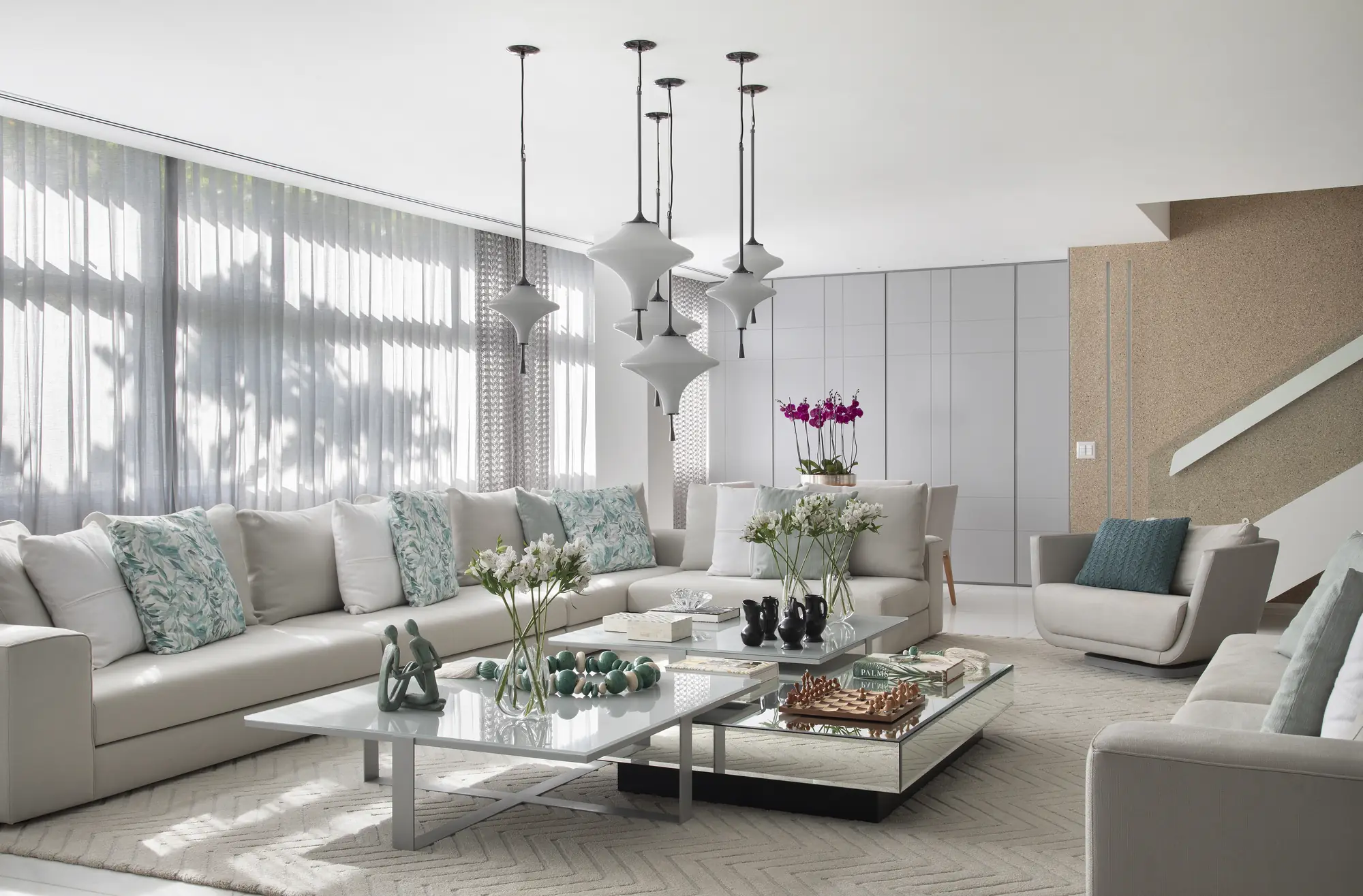 Living amplo com sofás claros, pendentes de vidro e cortinas