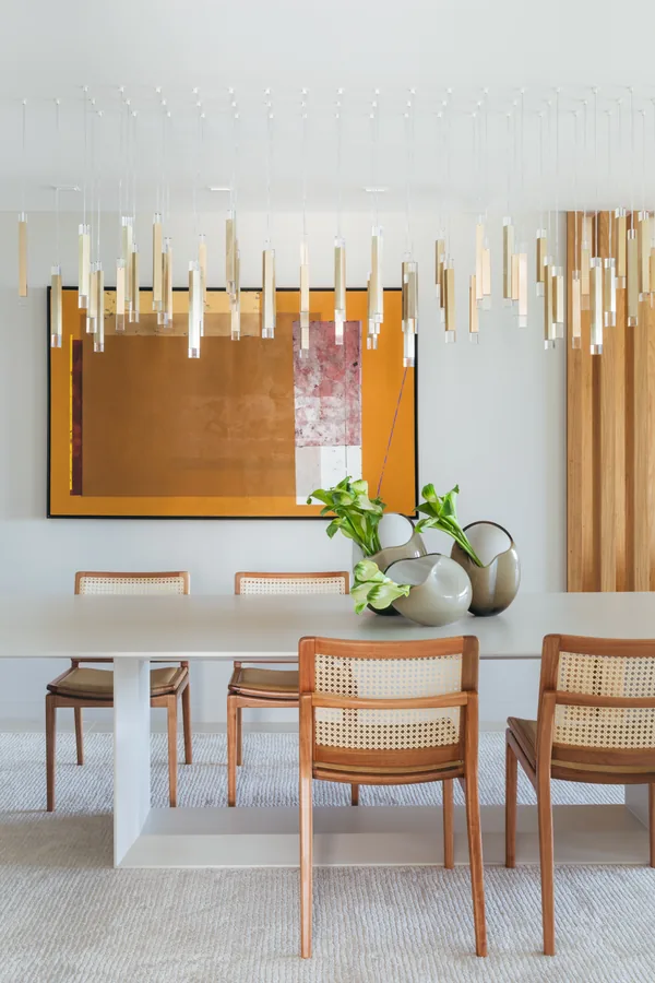 Sala de jantar com painel em madeira, lustre de pingentes e cadeiras de palhinha
