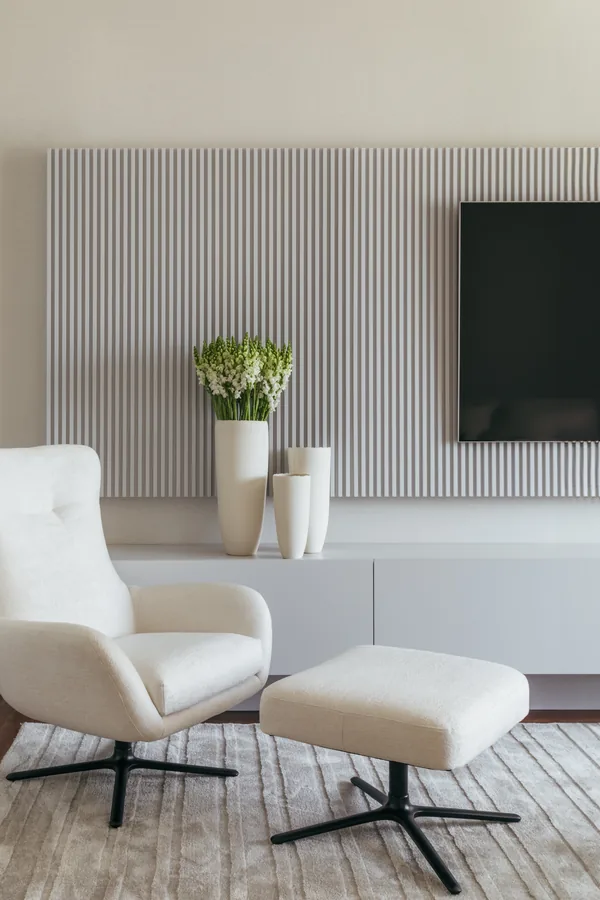 Sala de TV com painel ripado branco e poltrona com puff